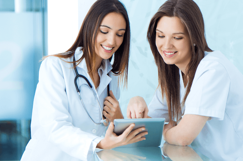 Photo of a smiling female doctor and nurse looking at a tablet and reviewing the data on it.